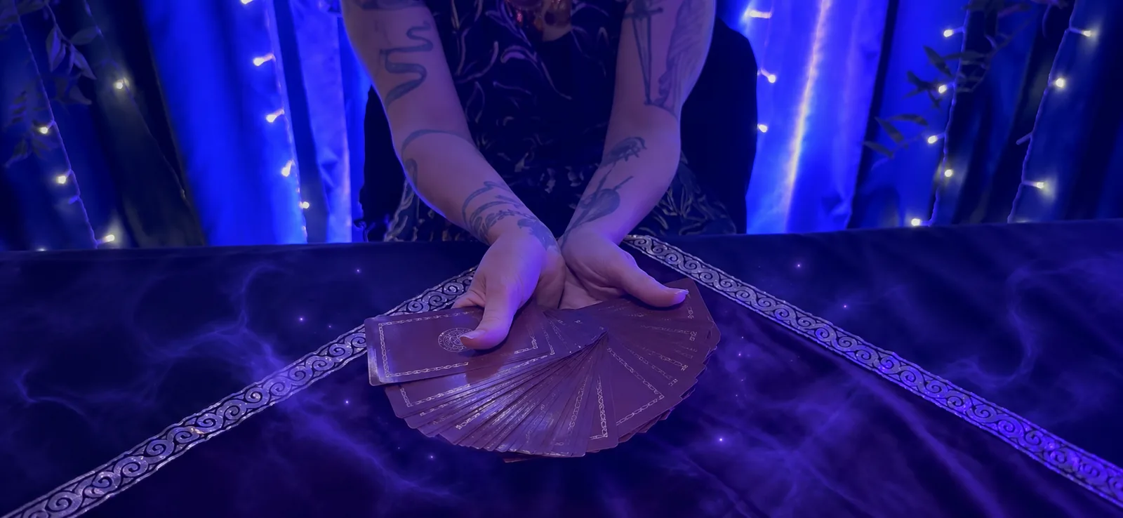 Crossed hands spreading tarot cards through violet mist and delicate lights