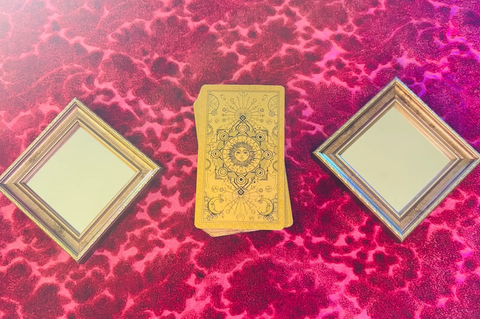 A golden tarot deck between two small mirrors on pink velvet