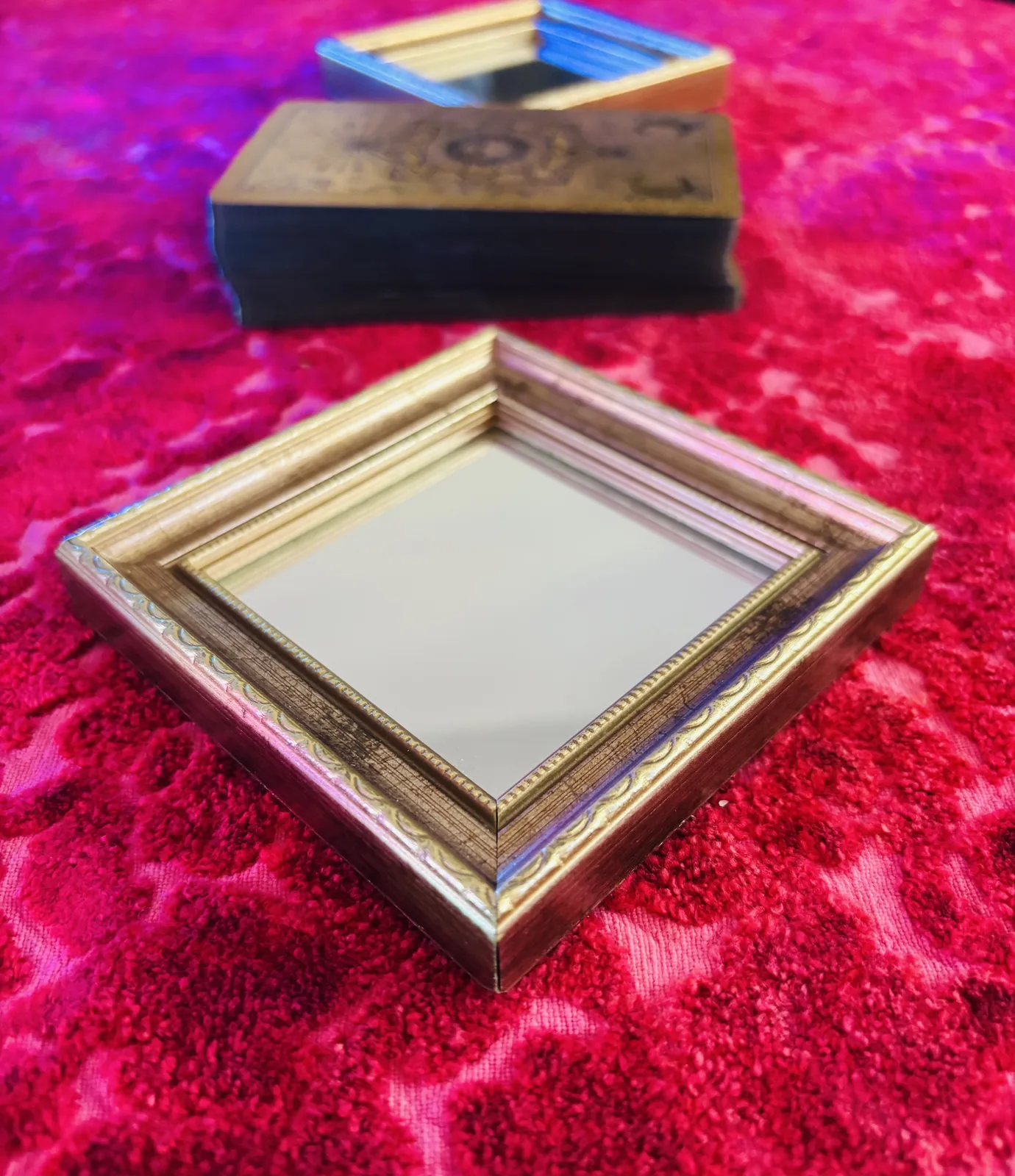 A small golden mirror and tarot deck on pink velvet